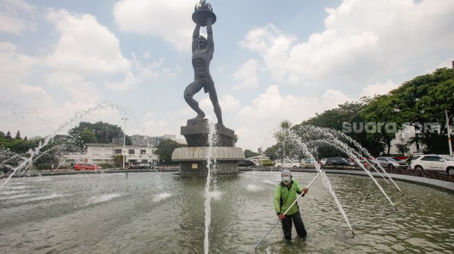 Petugas Dinas Pertamanan dan Kehutanan DKI Jakarta melakukan perwatan rutin kolam air mancur Patung Pemuda Membangun di Bundaran Senayan, Jakarta Pusat, Senin (2/8/2021). [Suara.com/Alfian Winanto]