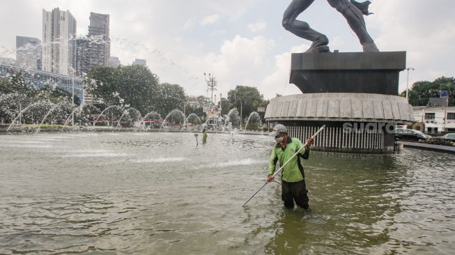 Petugas Dinas Pertamanan dan Kehutanan DKI Jakarta membersihkan bagian dasar kolam air mancur Patung Pemuda Membangun di Bundaran Senayan, Jakarta Pusat, Senin (2/8/2021). [Suara.com/Alfian Winanto]