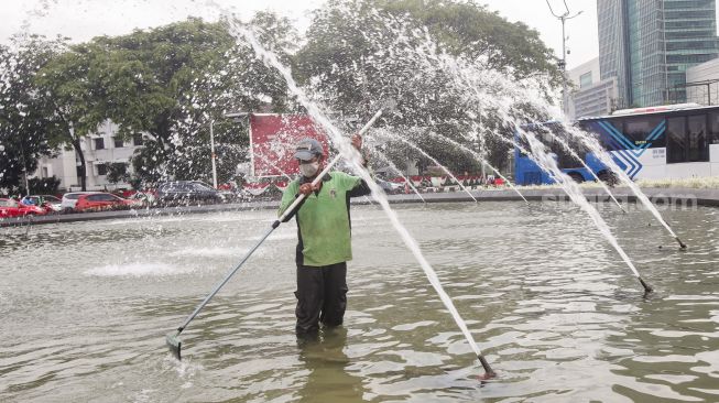 Petugas Dinas Pertamanan dan Kehutanan DKI Jakarta membersihkan bagian dasar kolam air mancur Patung Pemuda Membangun di Bundaran Senayan, Jakarta Pusat, Senin (2/8/2021). [Suara.com/Alfian Winanto]