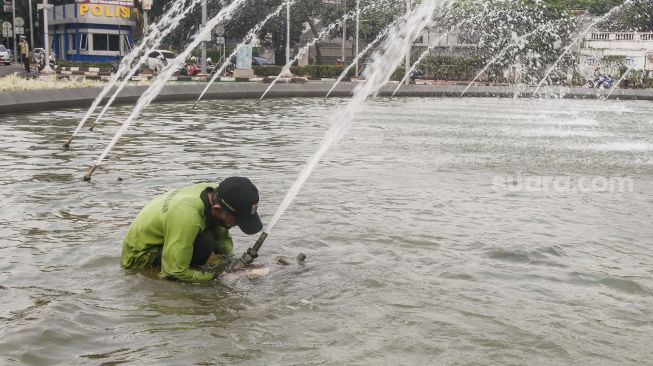 Petugas Dinas Pertamanan dan Kehutanan DKI Jakarta membersihkan bagian dasar kolam air mancur Patung Pemuda Membangun di Bundaran Senayan, Jakarta Pusat, Senin (2/8/2021). [Suara.com/Alfian Winanto]