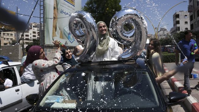 Siswa sekolah menengah Palestina merayakan kelulusan ujian akhir mereka yang dikenal sebagai "Tawjihi" di kota Hebron, Tepi Barat, Palestina, pada (3/8/2021). [HAZEM BADER / AFP]