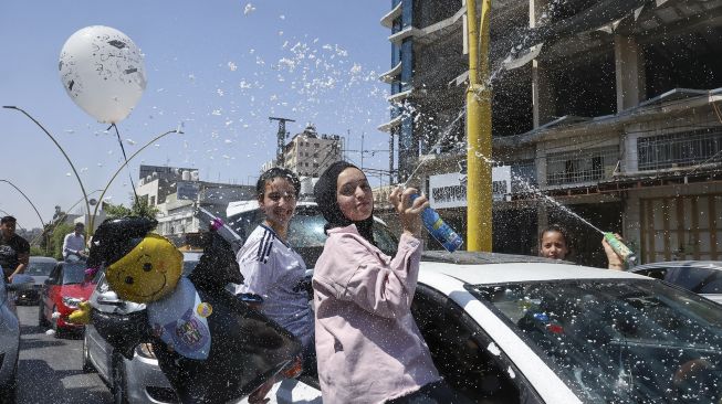 Siswa sekolah menengah Palestina menyemprotkan busa dari jendela mobil saat mereka merayakan di jalan setelah lulus ujian akhir mereka yang dikenal sebagai "Tawjihi" di kota Hebron, Tepi Barat, Palestina, pada (3/8/2021). [HAZEM BADER / AFP]