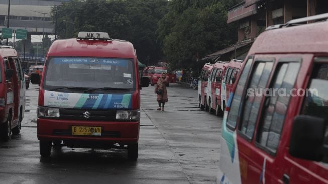 Seorang calon penumpang berjalan di dekat deretan angkutan umum kota (angkot) di Terminal Kampung Rambutan, Jakarta, Kamis (5/8/2021). [Suara.com/Angga Budhiyanto]