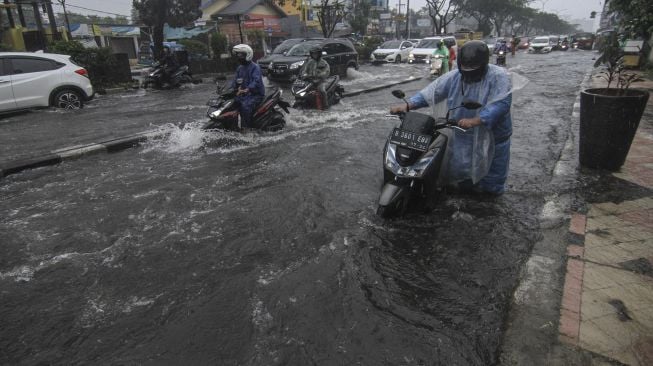 Pengendara mendorong sepeda motor yang mogok saat melintasi genangan air di Jalan Margonda Raya, Depok, Jawa Barat, Kamis (5/8/2021).  ANTARA FOTO/Asprilla Dwi Adha