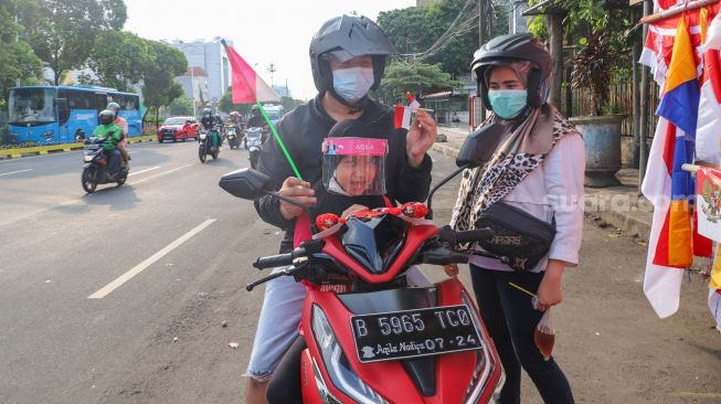 Warga menunjukkan pernak pernik bendera merah putih yang dibelinya di Jalan Matraman Raya, Jatinegara, Jakarta Timur, Minggu (8/8/2021). [Suara.com/Alfian Winanto]