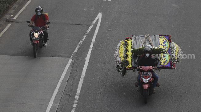 Pengendara sepeda motor membawa karangan bunga saat melintas di Jalan Gatot Subroto, Jakarta, Senin (9/8/2021). [Suara.com/Angga Budhiyanto]