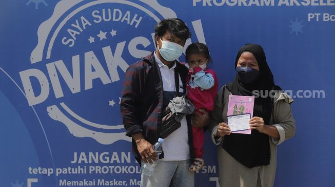 Seorang ibu hamil didampingi suami dan anaknya menunjukkan buku kesehatan ibu dan anak beserta surat keterangan vaksin usai mendapatkan vaksinasi COVID-19 di Gedung Wira Purusa LVRI DKI Jakarta, Kamis (12/8/2021). [Suara.com/Angga Budhiyanto]