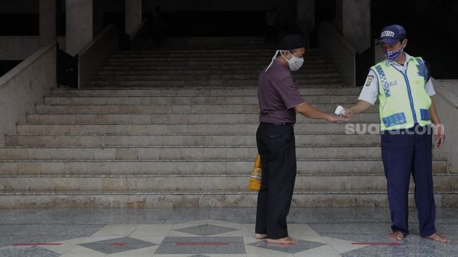 Petugas memeriksa suhu tubuh jamaah yang akan menunaikan sholat Jumat berjamaah di Masjid At-Tin, Jakarta, Jumat (13/8/2021). [Suara.com/Angga Budhiyanto]