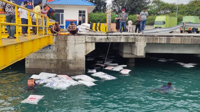 Petugas menyelamatkan pupuk muatan truk yang tercebur ke laut. [Suara.com/Adi Mulyadi]