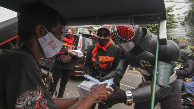 Relawan mengenakan kostum superhero satria baja hitam membagikan makanan dan masker kepada tukang becak di Grand Depok City, Depok, Jawa Barat, Jumat (13/8/2021). [ANTARA FOTO/Asprilla Dwi Adha]