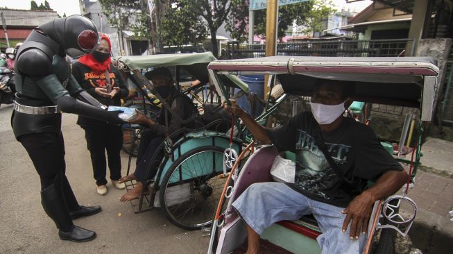 Relawan mengenakan kostum superhero satria baja hitam membagikan makanan dan masker kepada tukang becak di Grand Depok City, Depok, Jawa Barat, Jumat (13/8/2021). [ANTARA FOTO/Asprilla Dwi Adha]