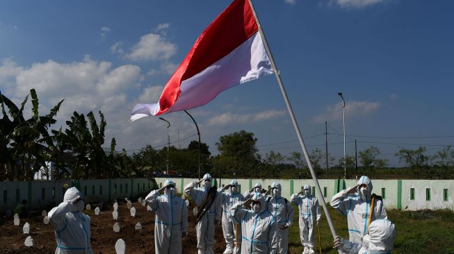 Sejumlah relawan pemakaman jenazah protokol COVID-19 dengan mengenakan Alat Pelindung Diri (APD) melakukan upacara bendera dalam rangka peringatan Hari Ulang Tahun ke-76 Proklamasi Kemerdekaan RI di Pemakaman Pagu Indah Kota Madiun, Jawa Timur, Minggu (15/8/2021).  ANTARA FOTO/Siswowidodo