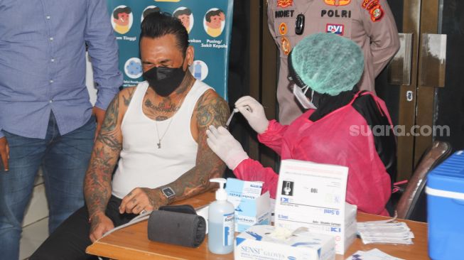 Ekspresi Musisi I Gede Ari Astina alias Jerinx SID saat menjalani vaksinasi Covid-19 di Polda Metro Jaya, Jakarta, Minggu (15/8/2021). [Suara.com/Alfian Winanto]
