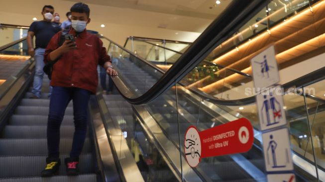 Warga menuruni eskalator yang dilengkapi teknologi sinar uv untuk sterilisasi di Pondok Indah Mall, Jakarta Selatan, Minggu (15/8/2021). [Suara.com/Alfian Winanto]