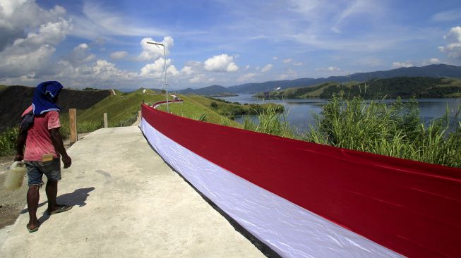 Seorang warga melintasi bendera Merah Putih yang dipasang di bukit Tungku Wiri atau Bukit Teletubies, Kampung Doyo Lama, Distrik Waibu, Kabupaten Jayapura, Papua, Senin (16/8/2021). ANTARA FOTO/Gusti Tanati 