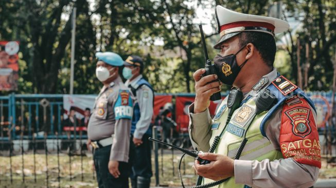 Seorang petugas kepolisian tengah menghimbau warga untuk turun sejenak dari kendaraan roda dua dan bersikap sempurna di Tugu TMP, Kota Tangerang Selasa 17 Agustus 2021. [Suara.com/ Hilal Rauda Fiqry]