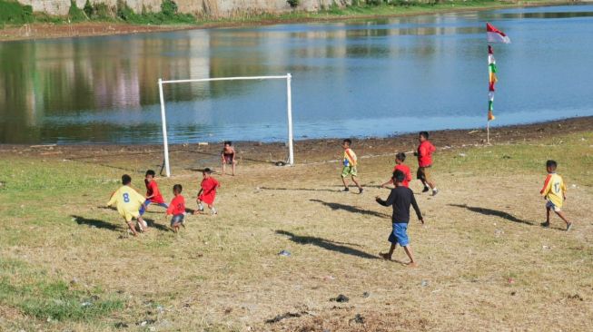 Warga bermain bola di Situ Ciburuy yang airnya menyusut, Rabu (18/8/2021). Situ yang terletak di Kabupaten Bandung Barat ini dibangun pada tahun 1800-an atas titah Ratu Belanda. [Suara.com/Ferrye Bangkit Rizki]