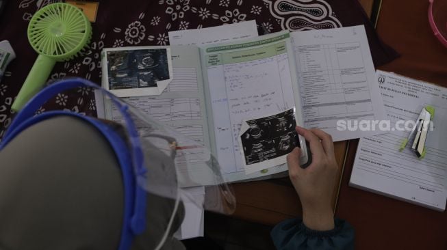 Petugas kesehatan memeriksa buku kesehatan ibu dan anak sebelum memberikan vaksinasi COVID-19 kepada ibu hamil di Kantor Kelurahan Cipayung, Jakarta, Kamis (19/8/2021). [Suara.com/Angga Budhiyanto]