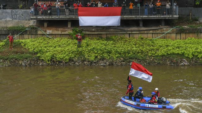 Gabungan relawan rescue mengibarkan bendera Merah Putih di Kali Ciliwung, Jakarta, Minggu (22/8/2021).