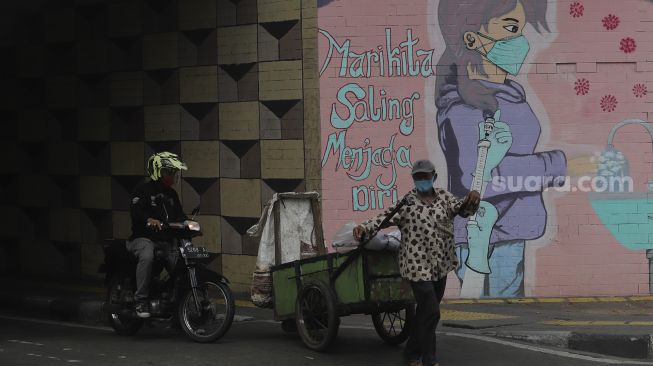 Warga berjalan di depan mural melawan COVID-19 di kawasan Cikokol, Cawang, Jakarta, Senin (23/8/2021). [Suara.com/Angga Budhiyanto]