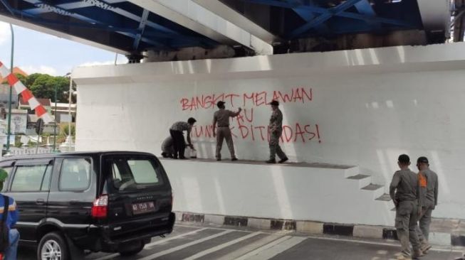  Petugas dari Satpol PP Kota Yogyakarta menghapus tulisan mural di Jembatan Kewek, Senin (23/08/2021). [Kontributor / Putu Ayu Palupi]