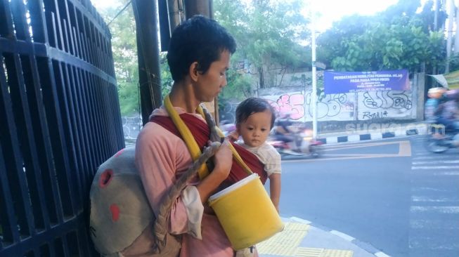 Badut jalanan sambil membawa anak saat meminta-minta kepada pengendara jalan di Jakarta. (Suara.com/Fakhri)