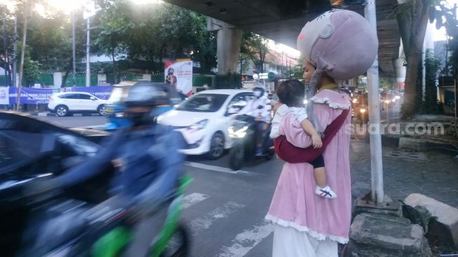 Badut jalanan sambil membawa anak saat meminta-minta kepada pengendara jalan di Jakarta. (Suara.com/Fakhri)