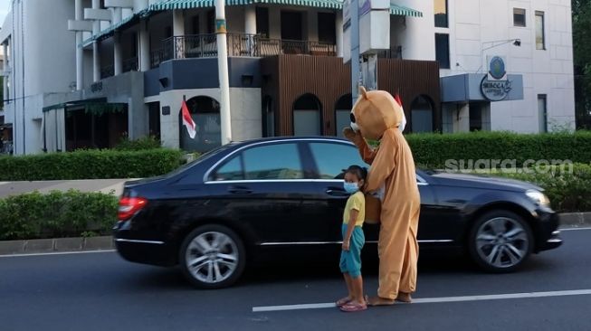 Badut jalanan sambil membawa anak saat meminta-minta kepada pengendara jalan di Jakarta. (Suara.com/Fakhri)