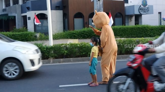 Badut jalanan sambil membawa anak saat meminta-minta kepada pengendara jalan di Jakarta. (Suara.com/Fakhri)