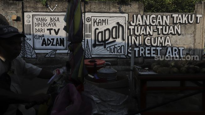 Warga berjalan di dekat mural yang bertuliskan "jangan takut tuan-tuan ini cuma street art" di Jakarta, Rabu (25/8/2021). [Suara.com/Angga Budhiyanto]