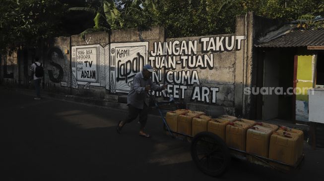 Warga berjalan di dekat mural yang bertuliskan "jangan takut tuan-tuan ini cuma street art" di Jakarta, Rabu (25/8/2021). [Suara.com/Angga Budhiyanto]