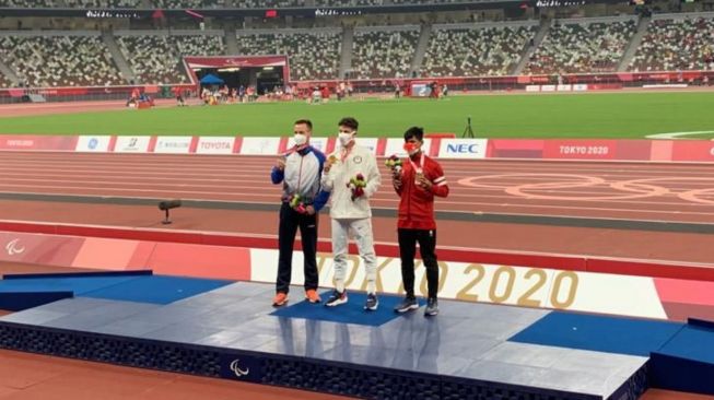 Atlet para-atletik Indonesia, Sapta Yogo Purnomo (kanan) saat berada di podium pasca meraih medali perunggu di nomor lari 100 meter putra kategori T37 Paralimpiade Tokyo 2020, Jumat (27/8/2021). [NPC Indonesia]