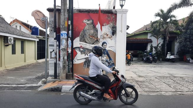 Seorang pengendara motor melintas di depan gambar mural yang terdapat di tembok di kawasan Kota Jogja, Jumat (27/8/2021). [Muhammad Ilham Baktora / SuaraJogja.id]