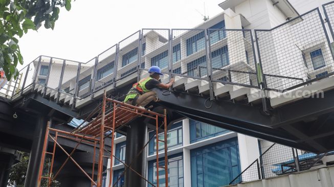 Pekerja menyelesaikan proyek pembangunan Jembatan Penyeberangan Orang (JPO) sekaligus Jembatan Penyeberangan Sepeda (JPS) Karet-Sudirman di Karet Tengsin, Jakarta Pusat, Sabtu (28/8/2021). [Suara.com/Alfian Winanto]