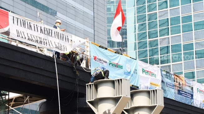 Pekerja menyelesaikan proyek pembangunan Jembatan Penyeberangan Orang (JPO) sekaligus Jembatan Penyeberangan Sepeda (JPS) Karet-Sudirman di Karet Tengsin, Jakarta Pusat, Sabtu (28/8/2021). [Suara.com/Alfian Winanto]