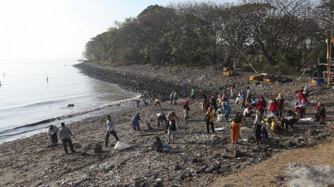 Warga memungut sampah di pinggir pantai kawasan Kedung Cowek, Surabaya, Jawa Timur, Minggu (29/8/2021). [ANTARA FOTO/Didik Suhartono]