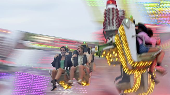 Pengunjung menikmati perjalanan pasar malam di Festival Musik Reading di London, Inggris, pada (27/8/2021). [DANIEL LEAL-OLIVAS / AFP]