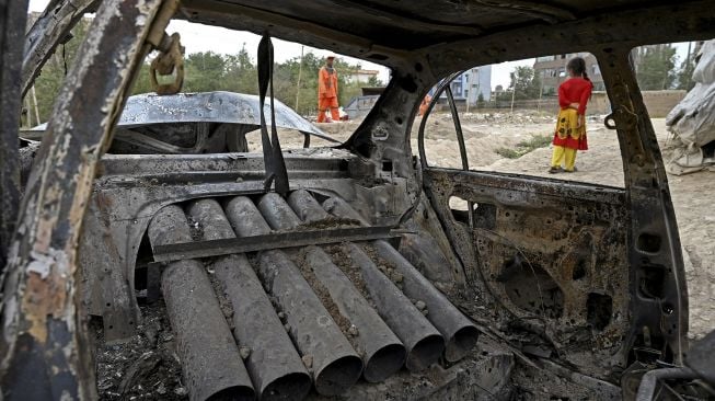 Seorang gadis berdiri di samping mobil yang rusak setelah beberapa roket ditembakkan di Kabul, Afghanistan, Senin (30/8/2021). [Wakil Kohsar / AFP]