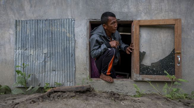 Seorang warga keluar dari rumahnya yang tertimbun lumpur melalui jendela akibat terjangan banjir bandang di Desa Rogo, Dolo Selatan, Sigi, Sulawesi Tengah, Senin (30/8/2021). [ANTARA FOTO/Basri Marzuki]