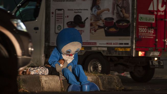 Pengamen badut, Fajar (17) menemani adiknya yang terlelap di pinggir Jalan TB Simatupang, Cilandak, Jakarta Selatan, Selasa (31/8/2021). ANTARA FOTO/Sigid Kurniawan