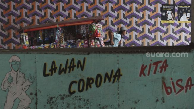 Pedagang keliling berjalan di dekat mural bertema COVID-19 di kolong Jalan Tol Lingkar Luar Jakarta, Cipayung, Jakarta Timur, Jumat (3/9/2021). [Suara.com/Angga Budhiyanto]