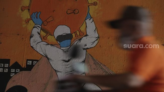 Pengendara sepeda motor melintas di dekat mural bertema COVID-19 di kolong Jalan Tol Lingkar Luar Jakarta, Cipayung, Jakarta Timur, Jumat (3/9/2021). [Suara.com/Angga Budhiyanto]