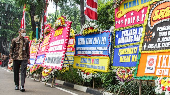 Pegawai gedung melihat karangan bunga yang terpajang di halaman kantor DPRD DKI Jakarta, Jakarta Pusat, Jumat (3/9/2021). [Suara.com/Alfian Winanto]