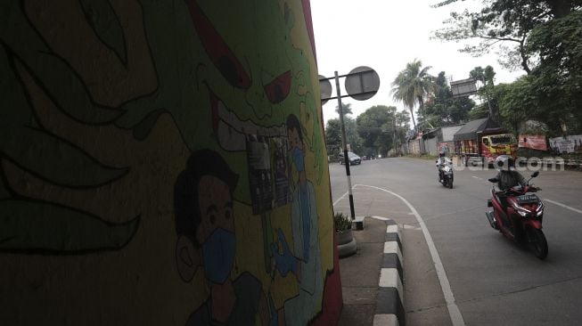 Pengendara sepeda motor melintas di dekat mural bertema COVID-19 di kolong Jalan Tol Lingkar Luar Jakarta, Cipayung, Jakarta Timur, Jumat (3/9/2021). [Suara.com/Angga Budhiyanto]