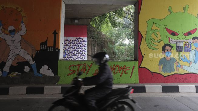 Pengendara sepeda motor melintas di dekat mural bertema COVID-19 di kolong Jalan Tol Lingkar Luar Jakarta, Cipayung, Jakarta Timur, Jumat (3/9/2021). [Suara.com/Angga Budhiyanto]