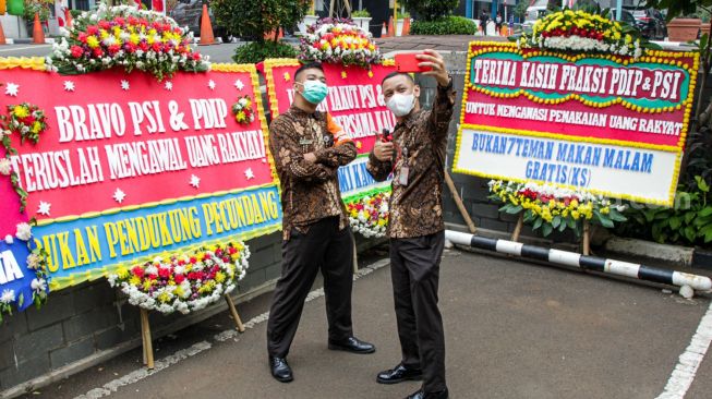 Pegawai gedung berswafoto di depan karangan bunga yang terpajang di halaman kantor DPRD DKI Jakarta, Jakarta Pusat, Jumat (3/9/2021). [Suara.com/Alfian Winanto]