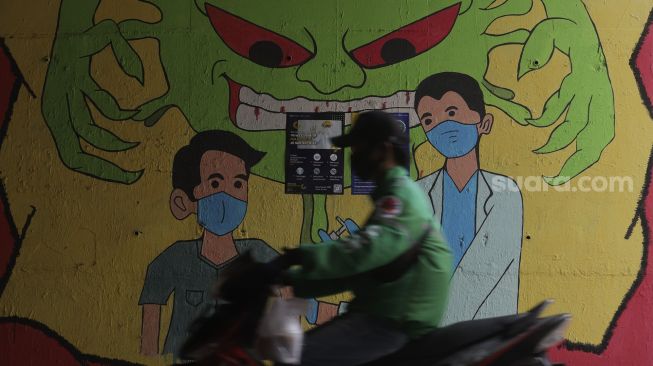 Pengendara sepeda motor melintas di dekat mural bertema COVID-19 di kolong Jalan Tol Lingkar Luar Jakarta, Cipayung, Jakarta Timur, Jumat (3/9/2021). [Suara.com/Angga Budhiyanto]