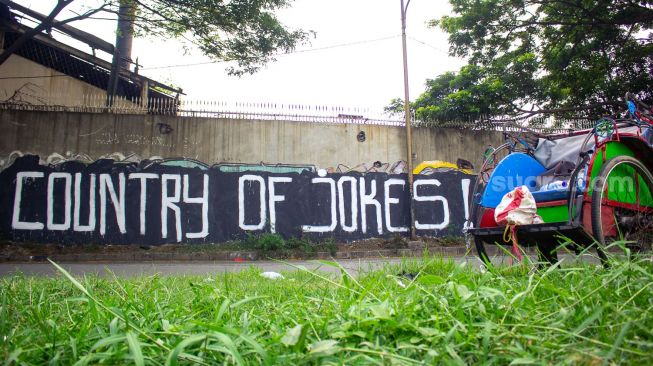 Becak terparkir didepan mural bertuliskan “ Country of Jokes” di Tangerang, Jumat (3/9).  ( Suara.com/Hilal Rauda Fiqry) 