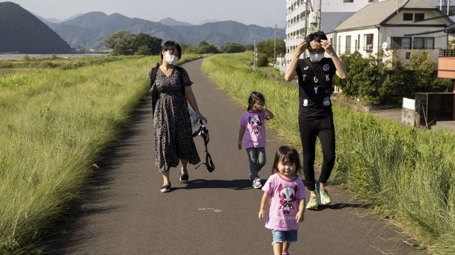 Pemain biola Jepang Manami Ito berjalan bersama suaminya Yuki (kanan) dan dua putri mereka Miu dan Mei dekat tempat tinggal mereka di Shizuoka, Jepang, pada (28/8/2021). [Yuki IWAMURA / AFP]