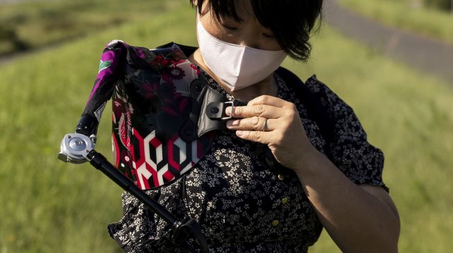 Musisi Jepang Manami Ito mengenakan lengan palsunya sebelum bermain biola selama sesi foto di Shizuoka, Jepang, pada (28/8/2021). [Yuki IWAMURA / AFP]